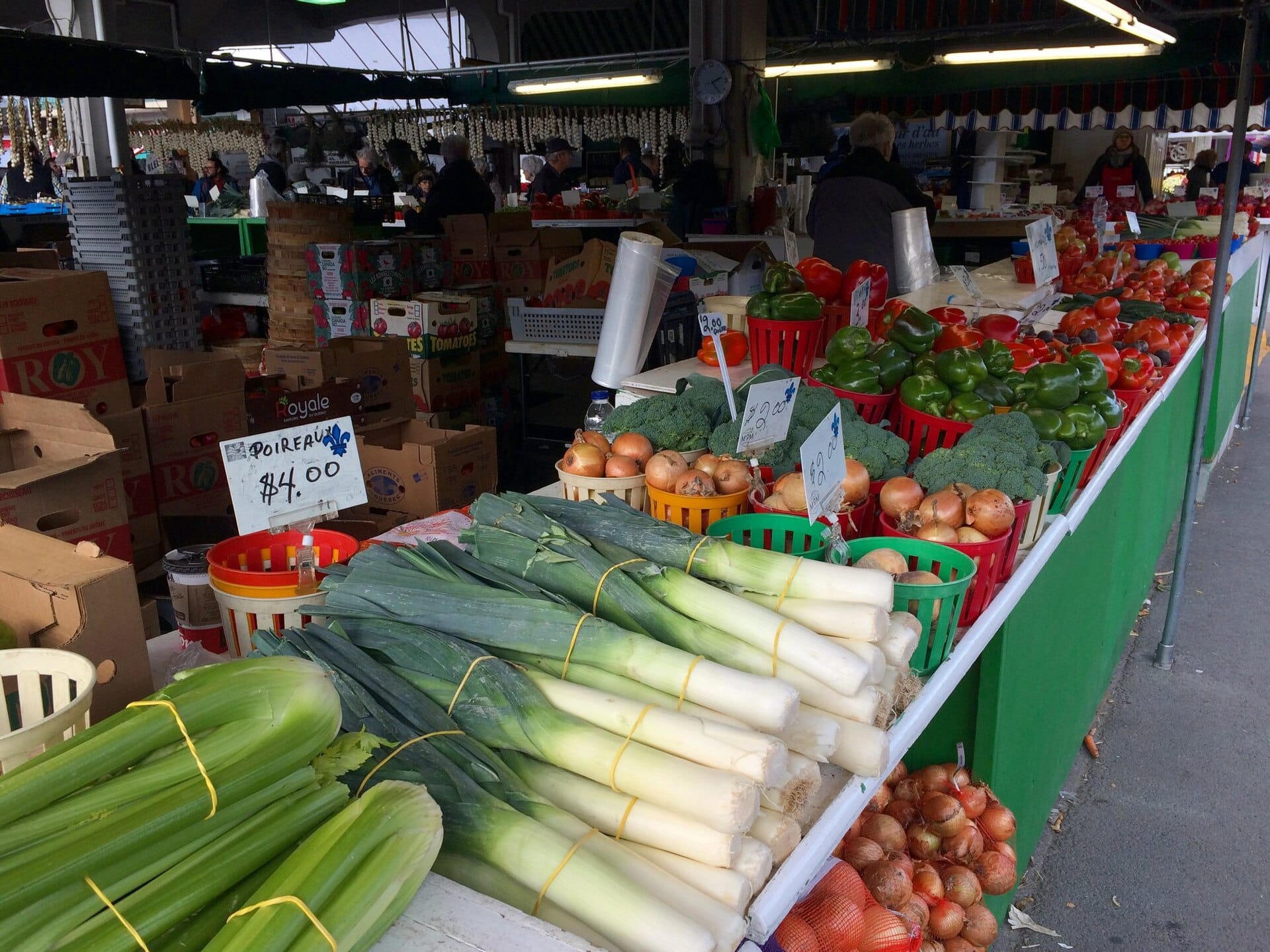 Des poireaux, des oignons, des brocolis et des poivrons sur un étal du marché Jean-Talon.